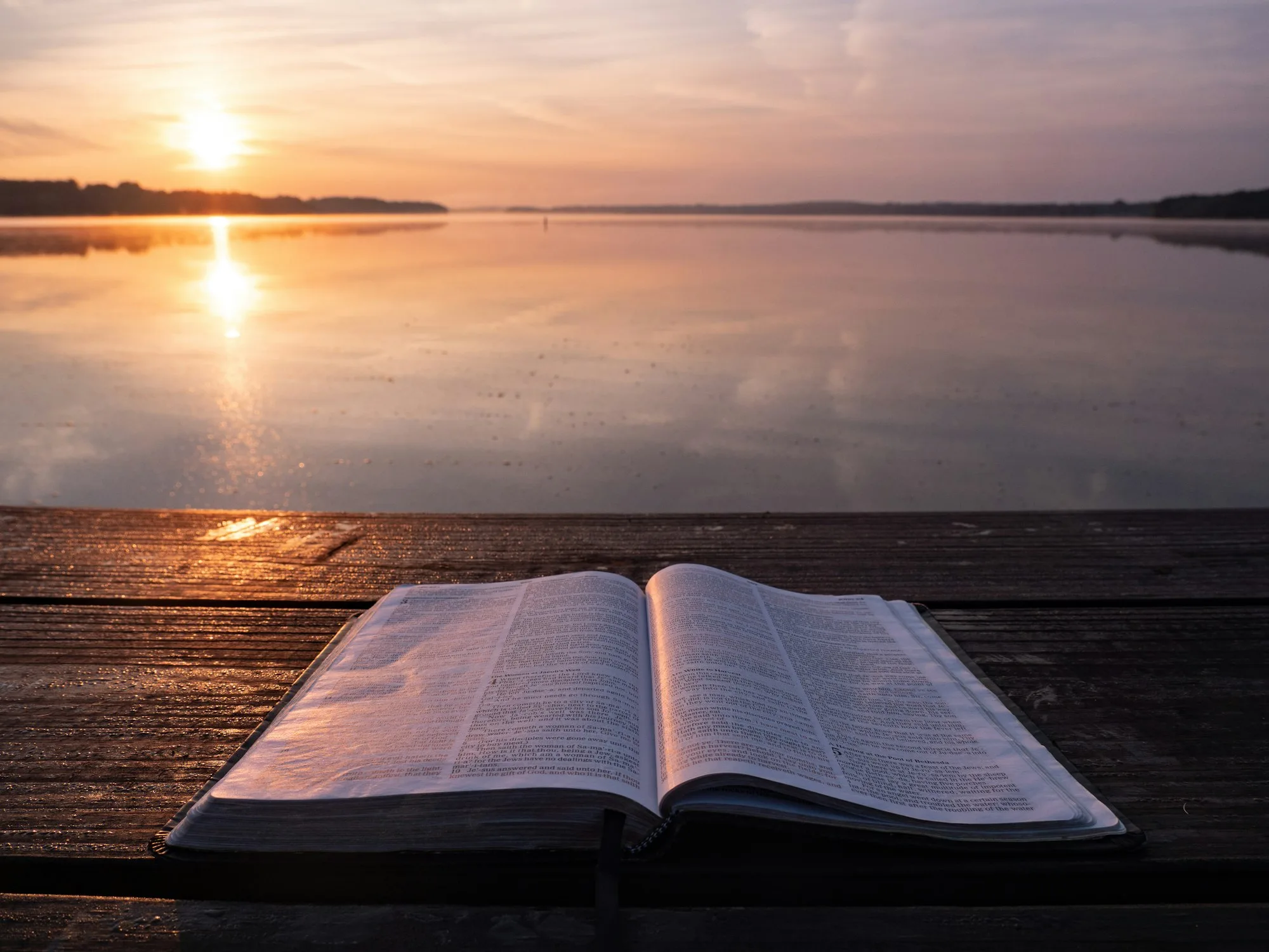 Open Bible on a dock by the water at sunset